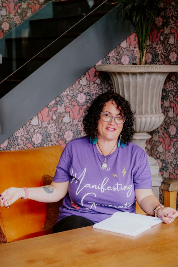 Jacqueline Kent is wearing a purple t shirt and smiling as she writes in her journal
